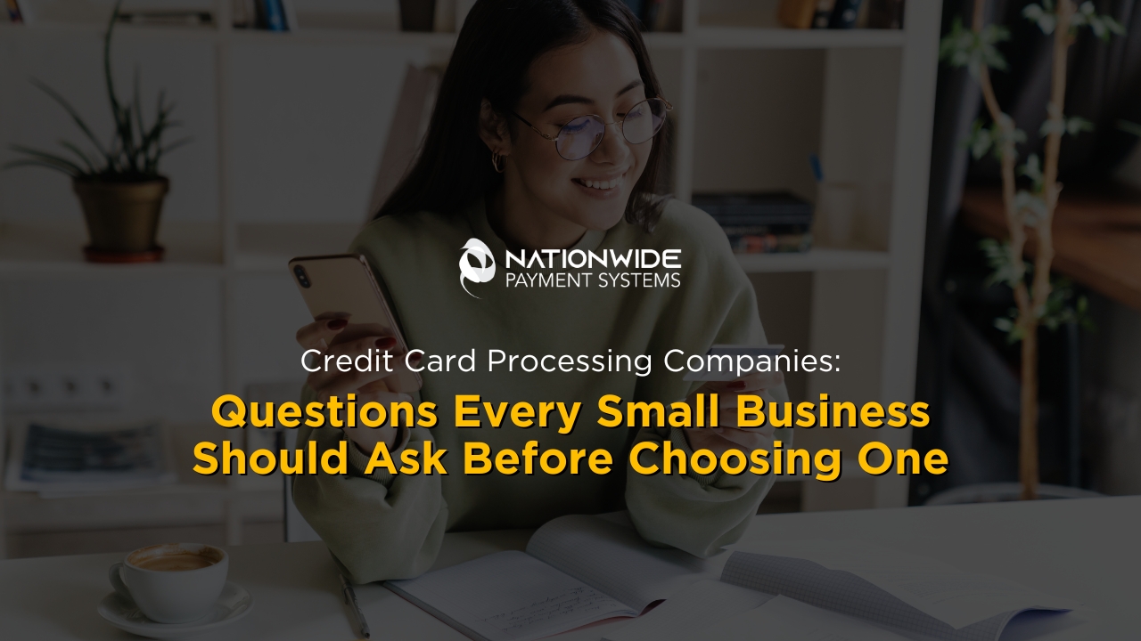 A small business owner smiling while looking closely at her credit card and using a smartphone to verify a transaction at a clean desk. An open notebook, a pen, and a ceramic cup of coffee sit in front of her. The white Nationwide Payment Systems logo is centered horizontally above bold yellow and white overlay text reading "Credit Card Processing Companies: Questions Every Small Business Should Ask Before Choosing One."
